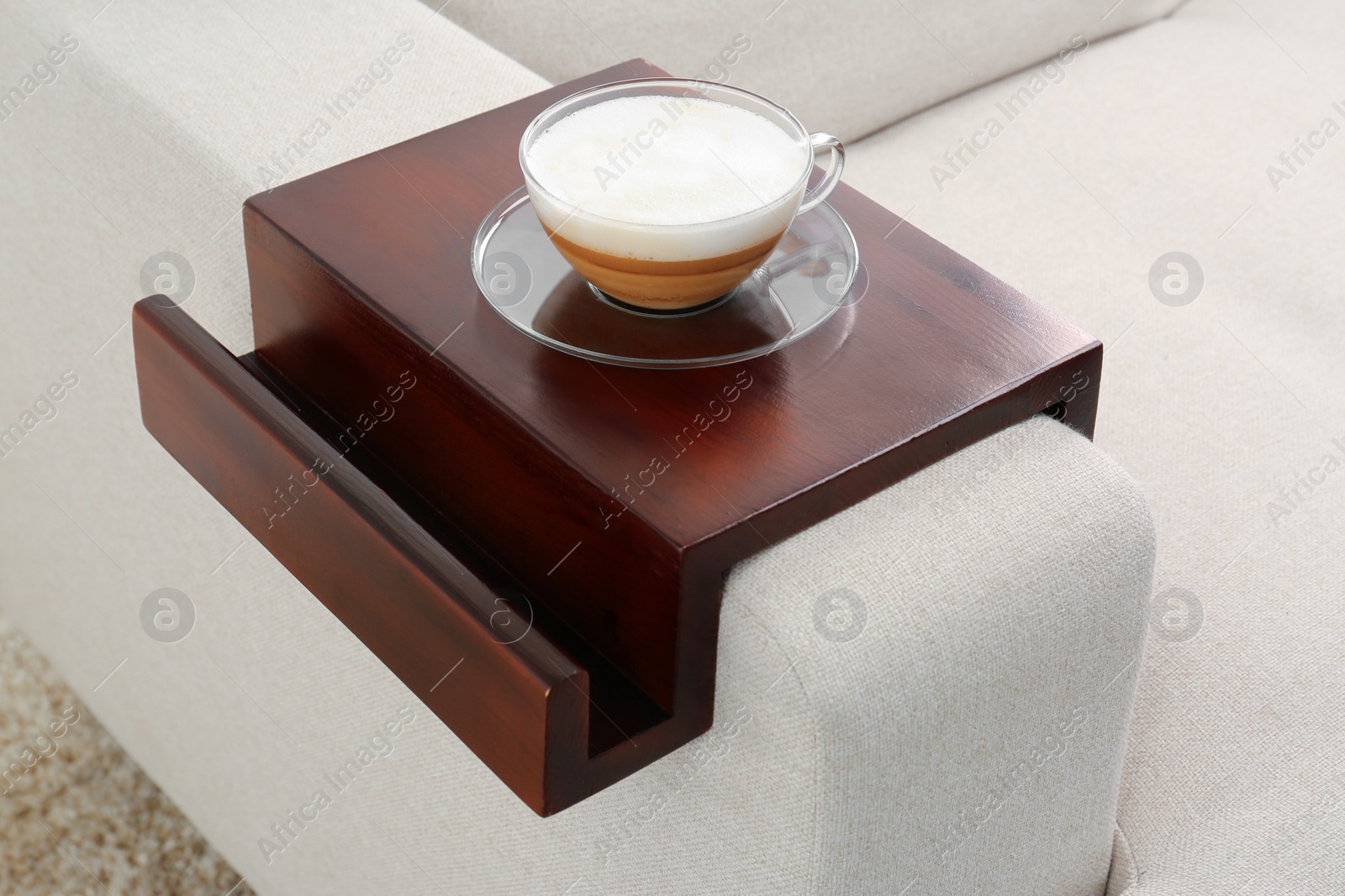 Photo of Cup of coffee on sofa with wooden armrest table indoors. Interior element