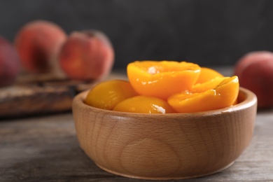 Photo of Bowl with conserved peach halves on wooden table. Space for text