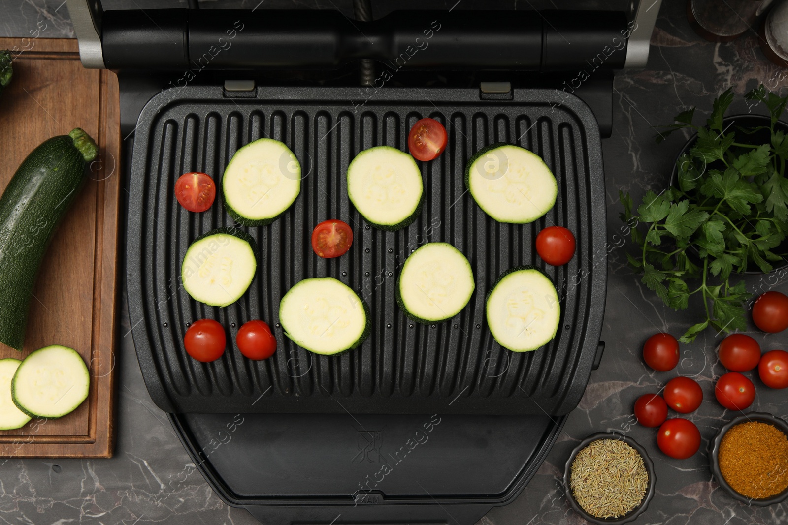 Photo of Electric grill with vegetables and spices on black marble table, flat lay