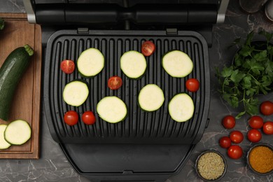 Photo of Electric grill with vegetables and spices on black marble table, flat lay