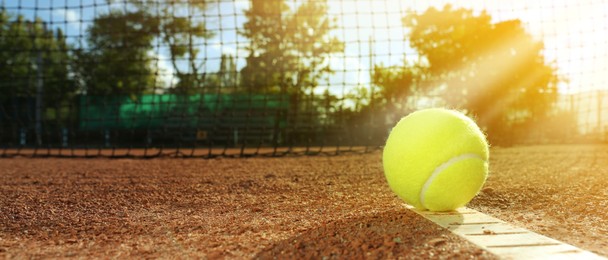 Image of Bright yellow tennis ball on clay court, space for text. Banner design