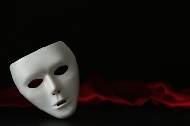 Photo of White theatre mask and red fabric on black background, space for text