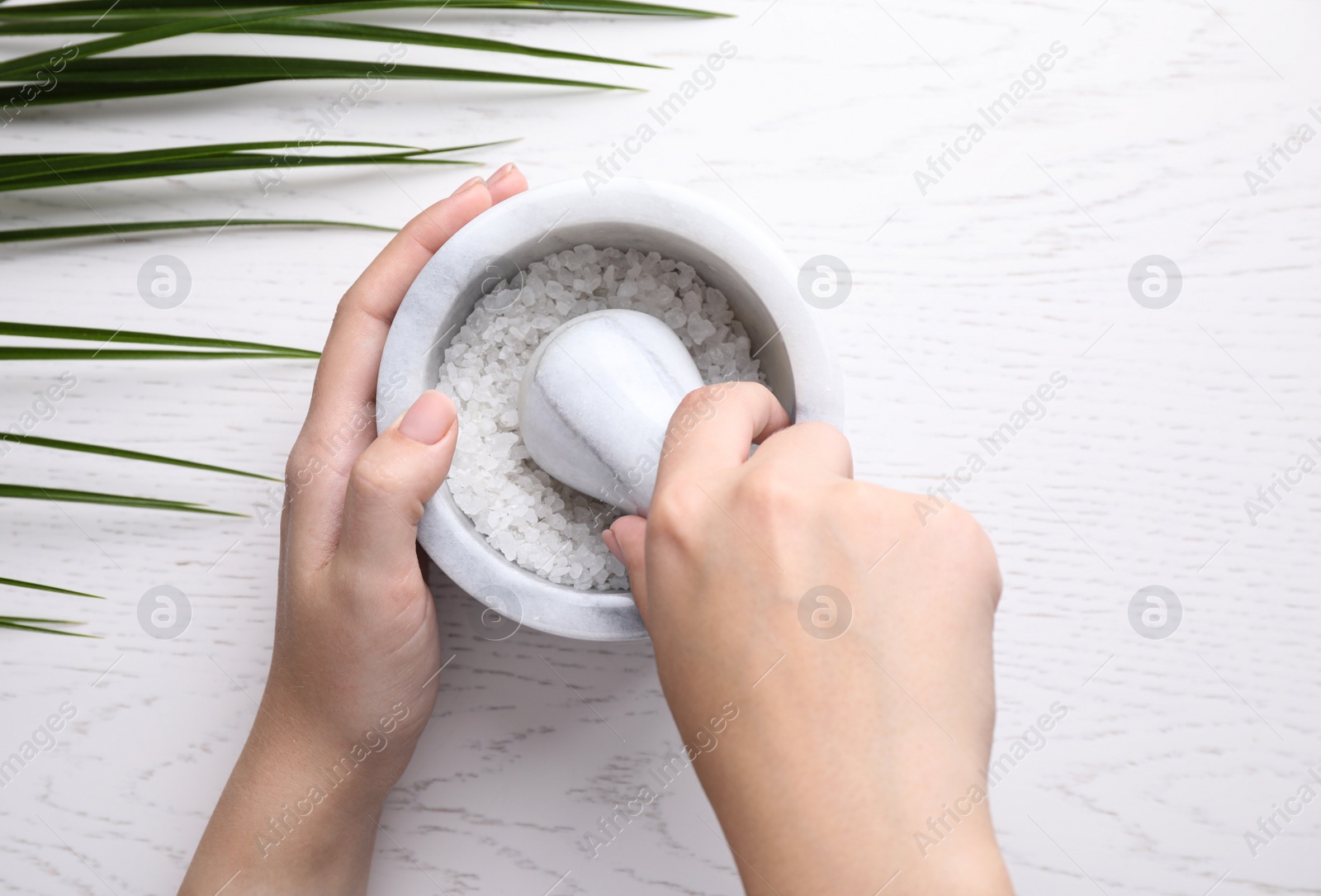 Photo of Woman with sea salt on white wooden background, top view. Spa treatment