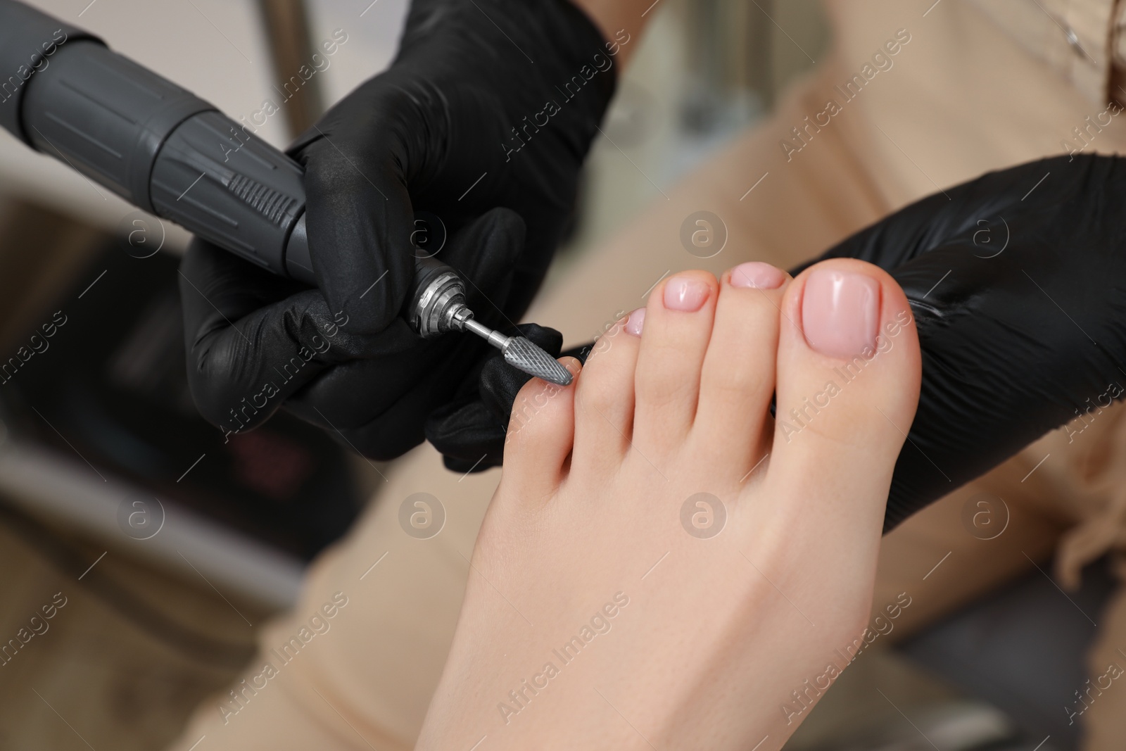 Photo of Professional master making hardware pedicure for client in beauty salon, closeup