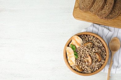 Photo of Tasty buckwheat porridge with meat on white wooden table, flat lay. Space for text