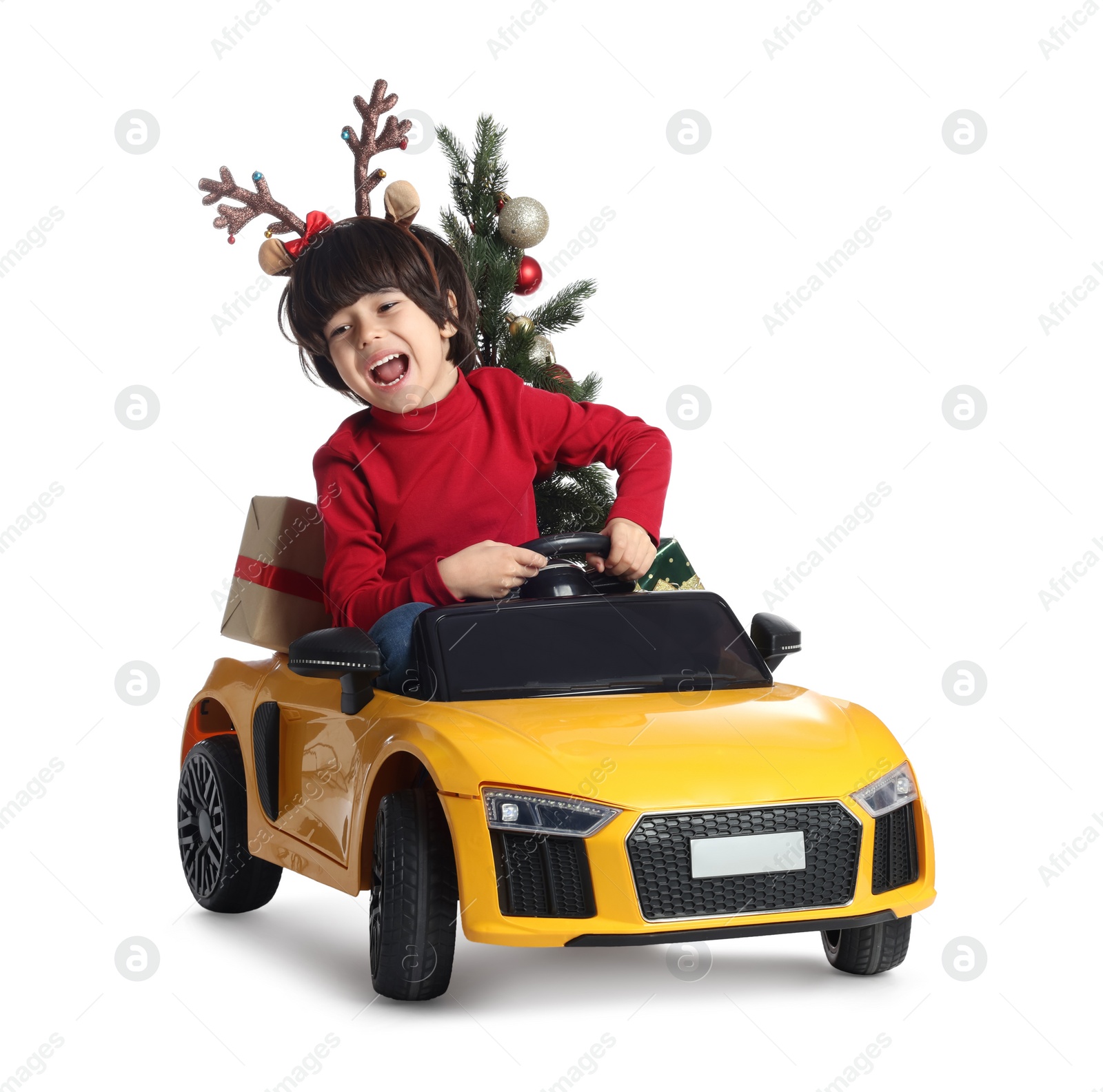 Photo of Cute little boy with Christmas tree and gift box driving children's electric toy car on white background