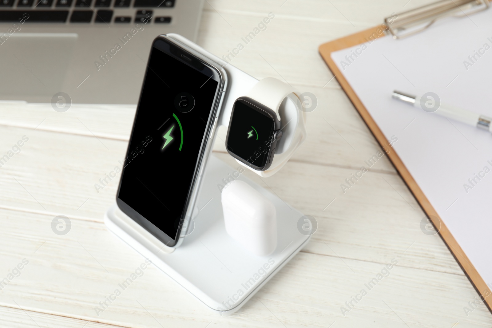 Photo of Set of gadgets charging with wireless device on white wooden table