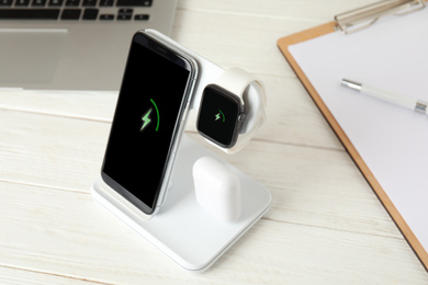 Set of gadgets charging with wireless device on white wooden table