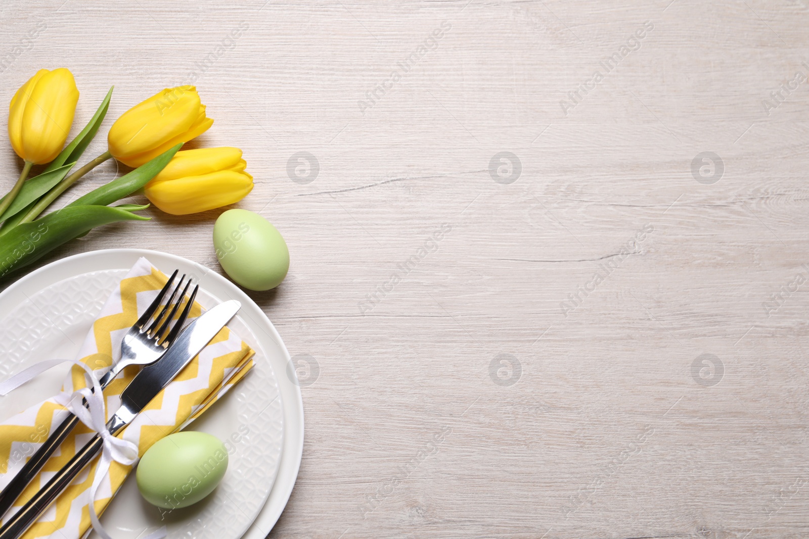 Photo of Festive Easter table setting with eggs and flowers on light wooden background, flat lay. Space for text