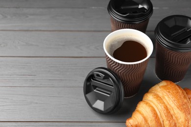Coffee to go. Paper cups with tasty drink and croissant on grey wooden table. Space for text