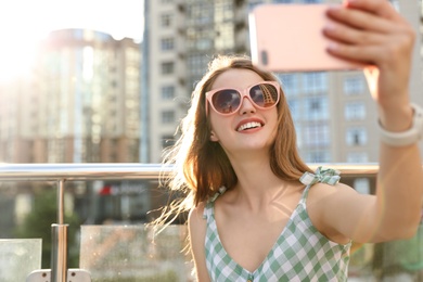Beautiful young woman with sunglasses taking selfie outdoors, space for text