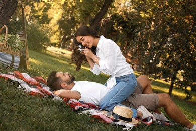 Photo of Woman taking picture of her boyfriend on picnic plaid in summer park