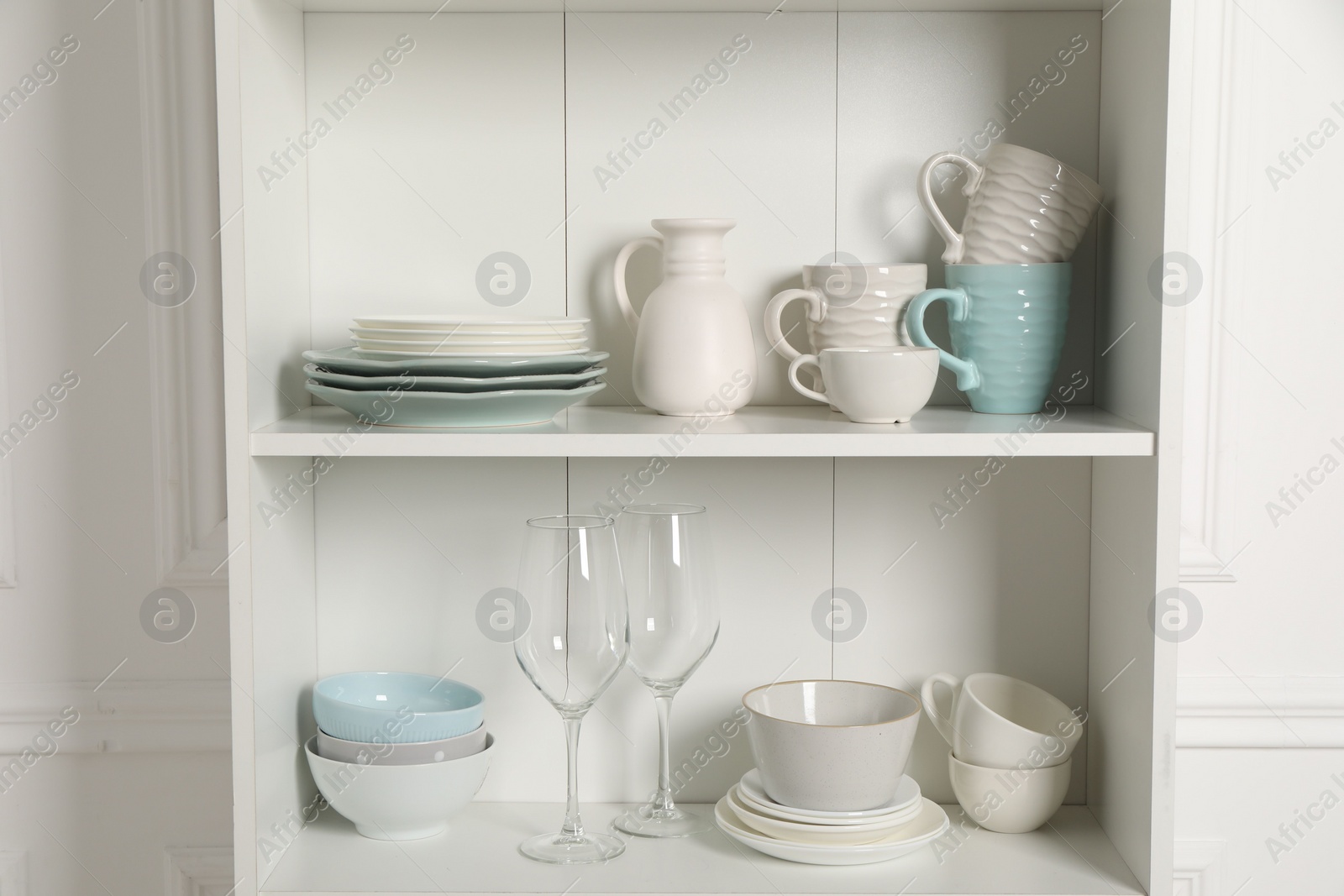 Photo of Different clean dishware and glasses on shelves in cabinet indoors