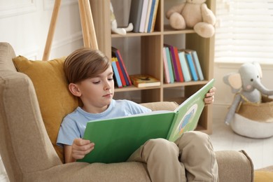 Photo of Little boy reading book in armchair at home