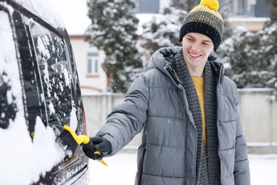 Photo of Man cleaning snow from car window outdoors