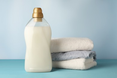 Photo of Bottle of fabric softener and towels on light blue table