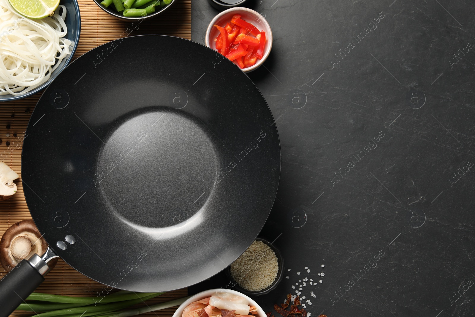 Photo of Flat lay composition with black wok, spices and products on dark textured table. Space for text