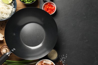 Flat lay composition with black wok, spices and products on dark textured table. Space for text