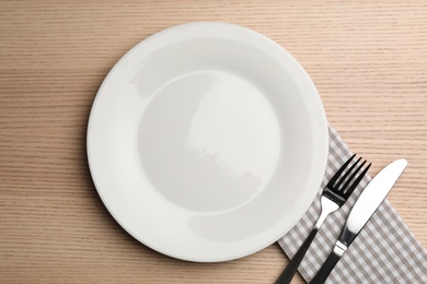 Photo of Empty plate, cutlery and napkin on wooden background, flat lay