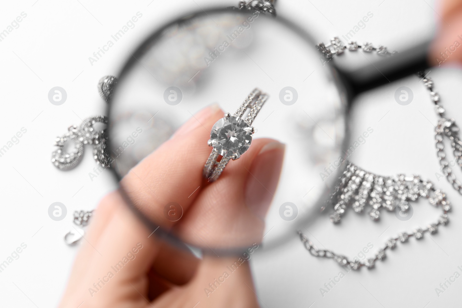 Photo of Jeweler examining diamond ring with magnifying glass at white table, closeup