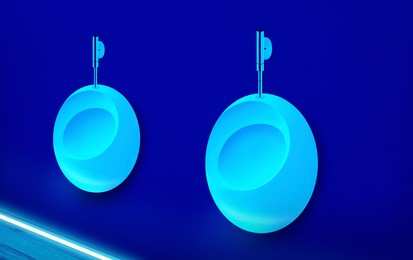 Ceramic urinals in men's public restroom lit with UV blue light