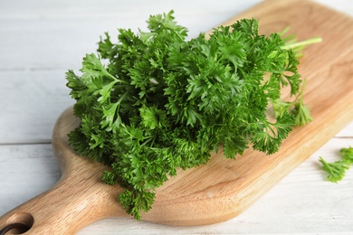 Photo of Wooden board with fresh green parsley on table