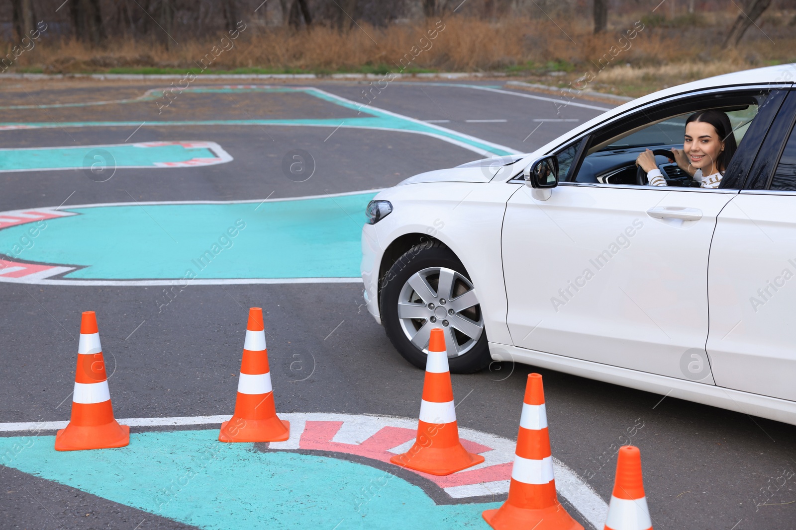 Photo of Young woman in car on test track with traffic cones. Driving school