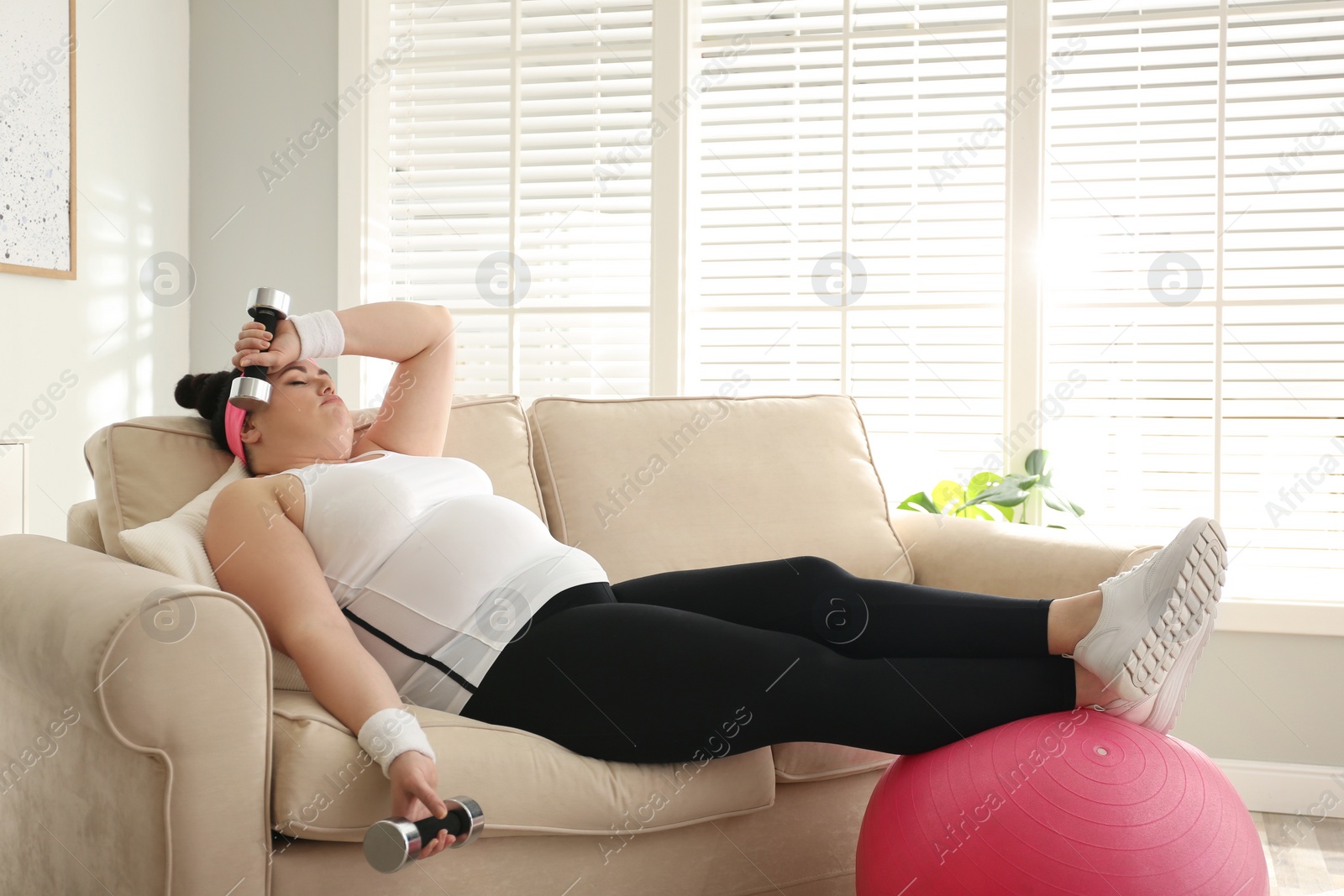 Photo of Lazy overweight woman with sport equipment on sofa at home