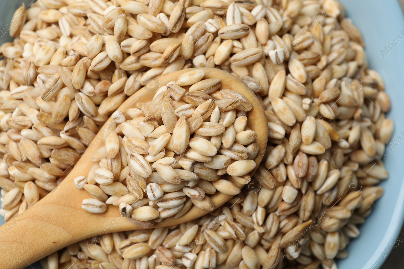 Photo of Wooden spoon with dry pearl barley in bowl, top view