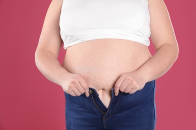 Overweight woman trying to wear tight jeans on color background, closeup