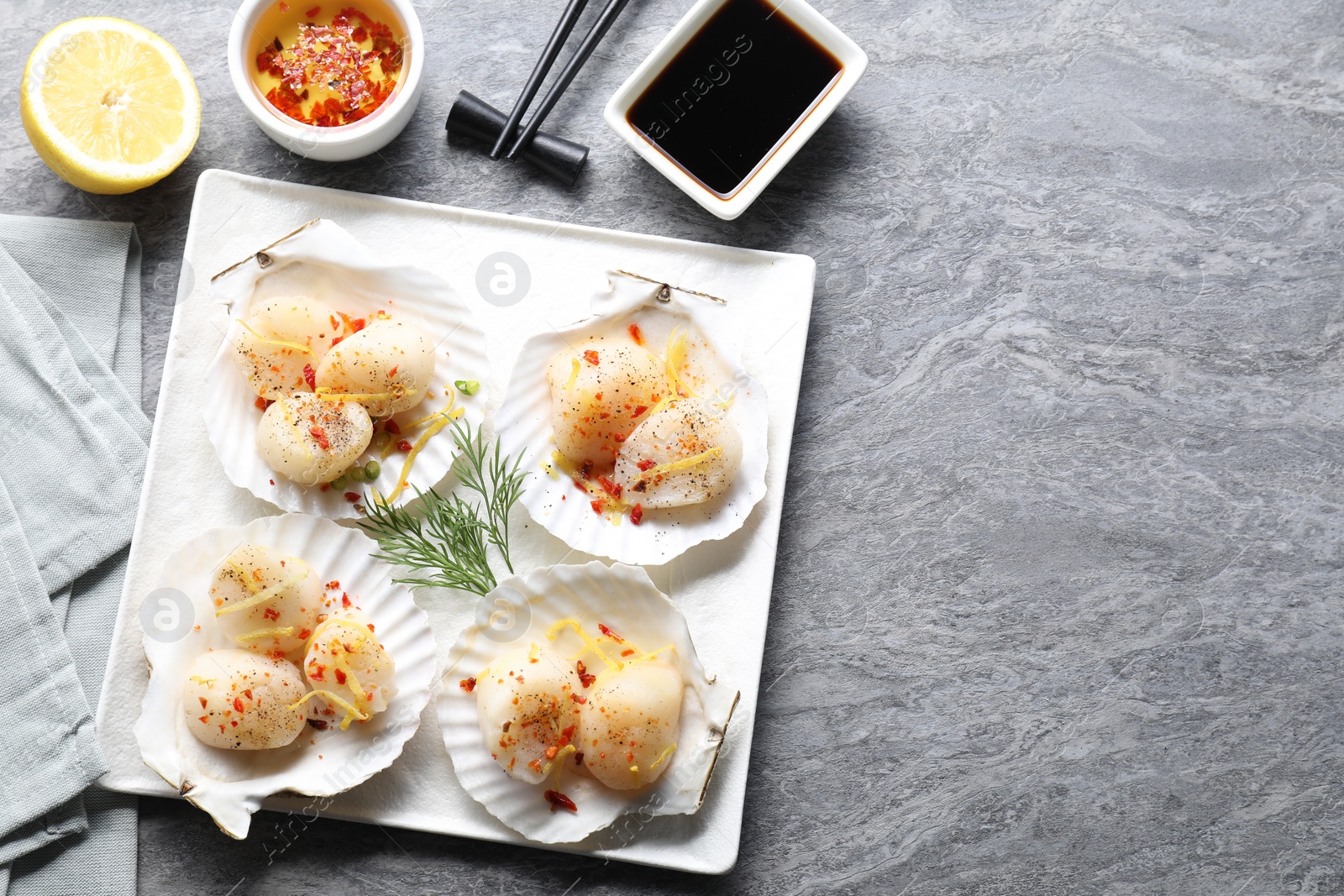 Photo of Raw scallops with spices, lemon zest, shells and sauces on grey marble table, flat lay. Space for text