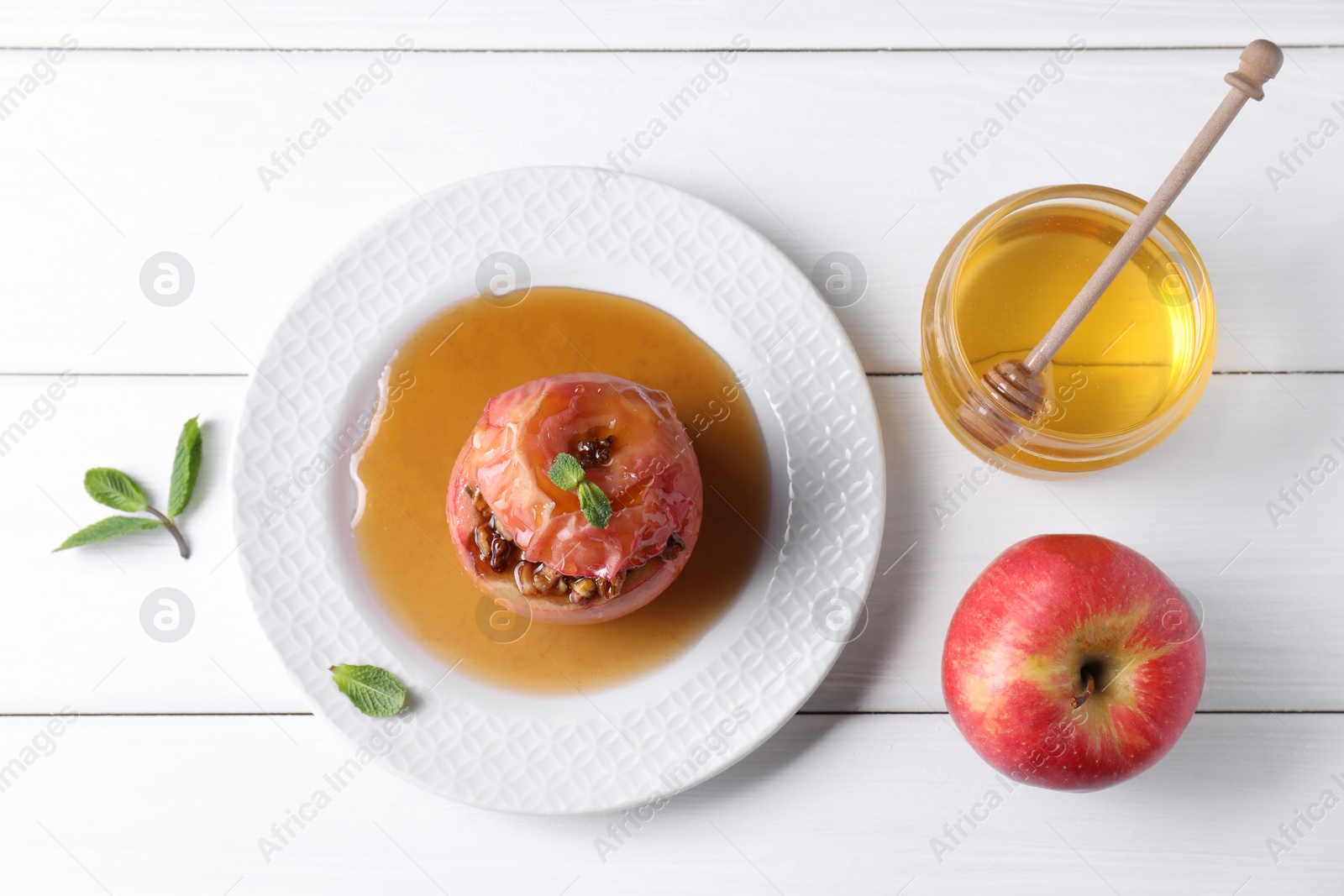 Photo of Tasty baked apple with nuts, honey and mint on white wooden table, flat lay