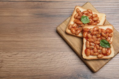 Photo of Toasts with delicious canned beans on wooden table, top view. Space for text