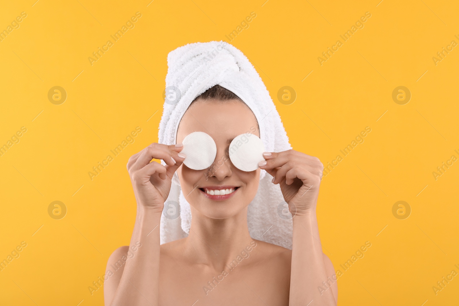 Photo of Smiling woman removing makeup with cotton pads on yellow background