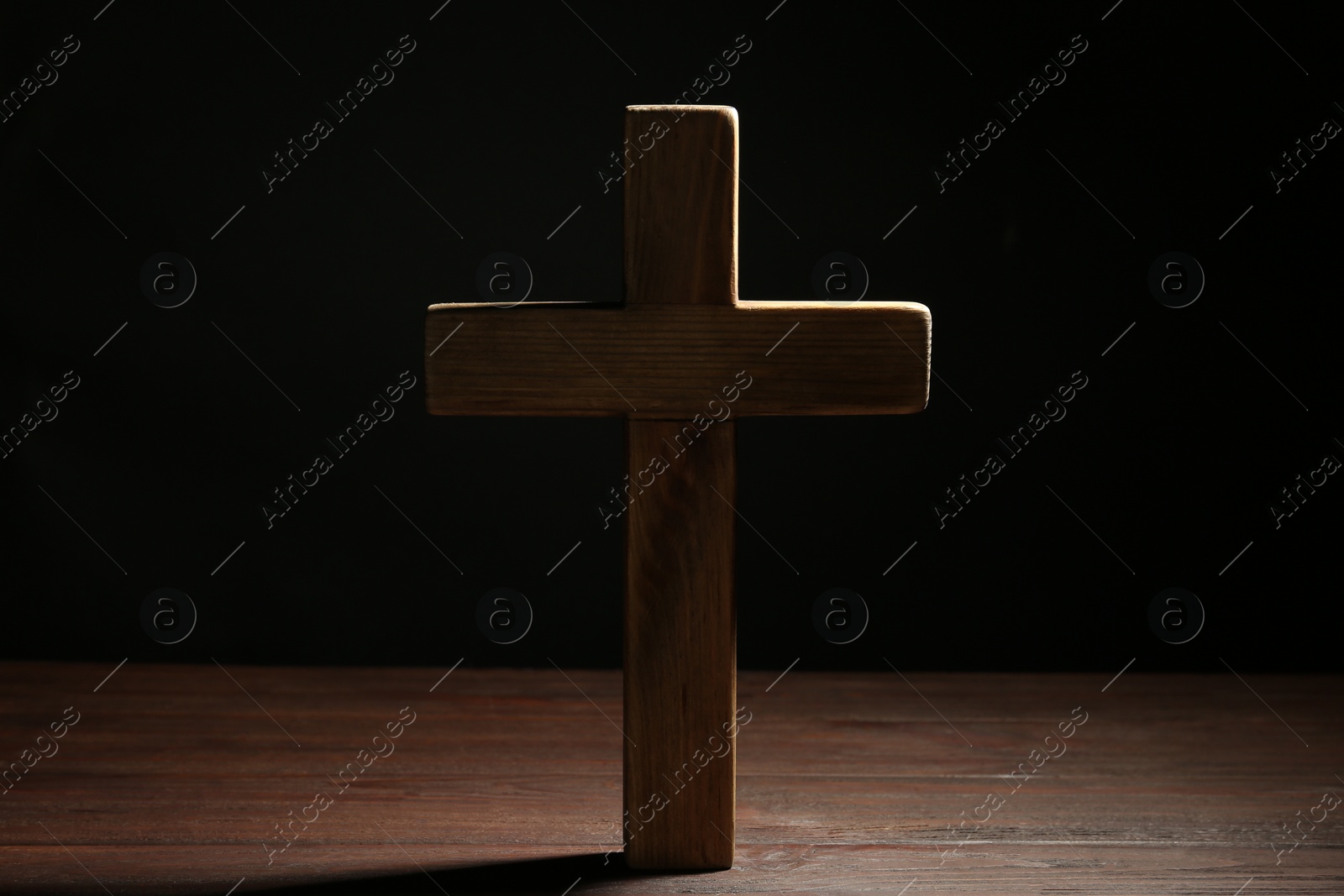 Photo of Christian cross on wooden table against black background. Religion concept