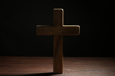 Photo of Christian cross on wooden table against black background. Religion concept