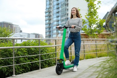 Happy woman with modern electric kick scooter on city street, space for text