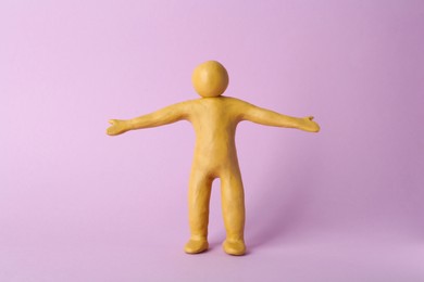 Photo of Human figure with arms wide open made of yellow plasticine on violet background