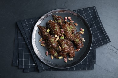 Delicious baklava with pistachio nuts and napkin on black table, top view