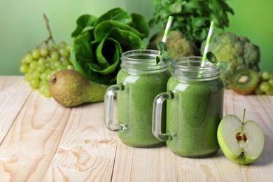 Mason jars of fresh green smoothie and ingredients on wooden table. Space for text