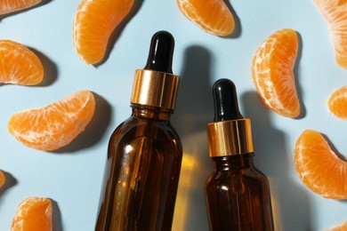 Aromatic tangerine essential oil in bottles and citrus fruits on light blue table, flat lay