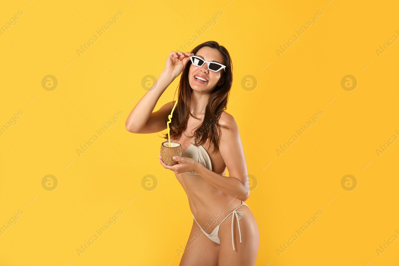 Photo of Beautiful woman in stylish bikini with tropical cocktail on yellow background