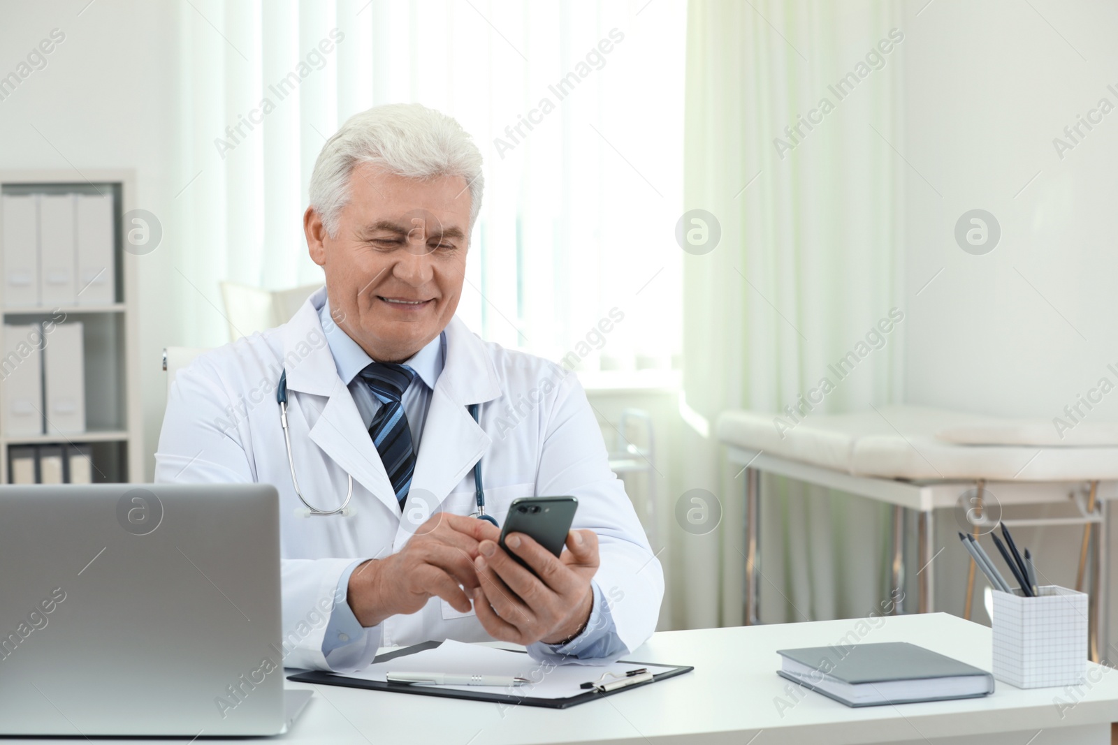 Photo of Senior doctor with smartphone at table in office