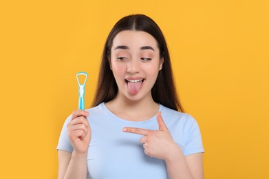 Happy woman showing tongue cleaner on yellow background