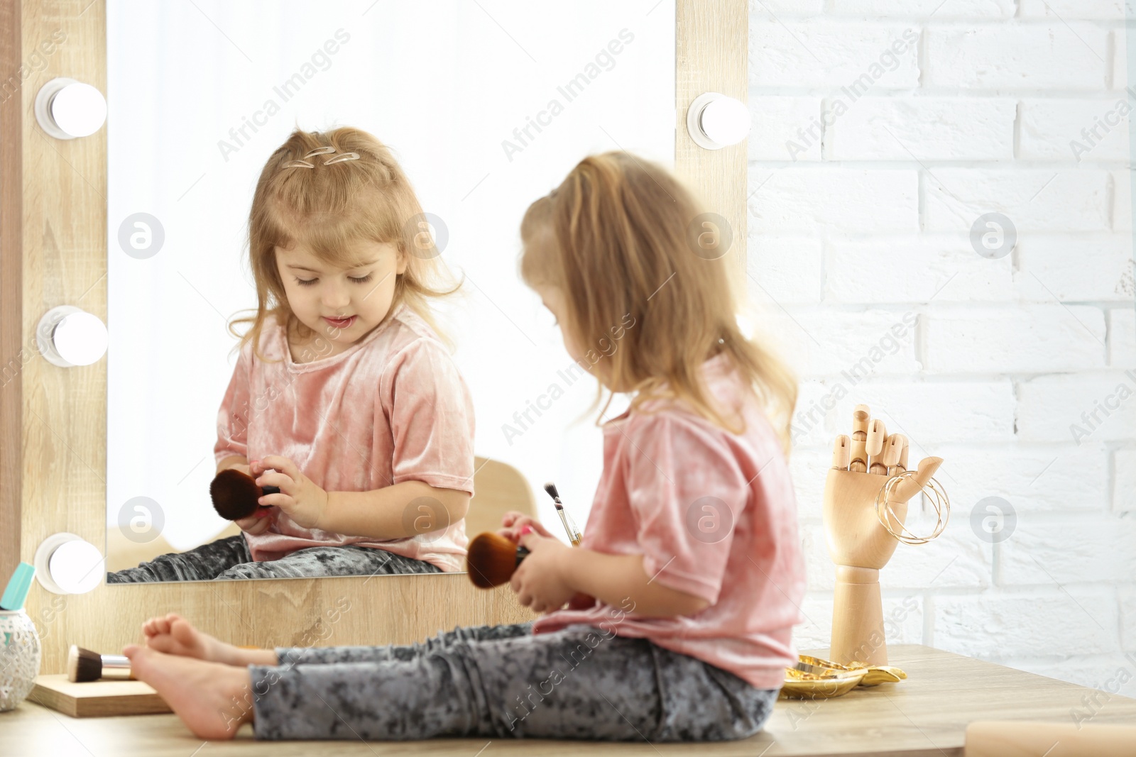 Photo of Cute little girl playing with cosmetics in dressing room