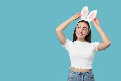 Photo of Happy woman wearing bunny ears headband on turquoise background, space for text. Easter celebration