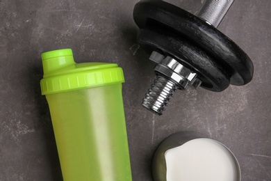 Photo of Bottle with protein shake, jug of milk and dumbbell on grey background, top view