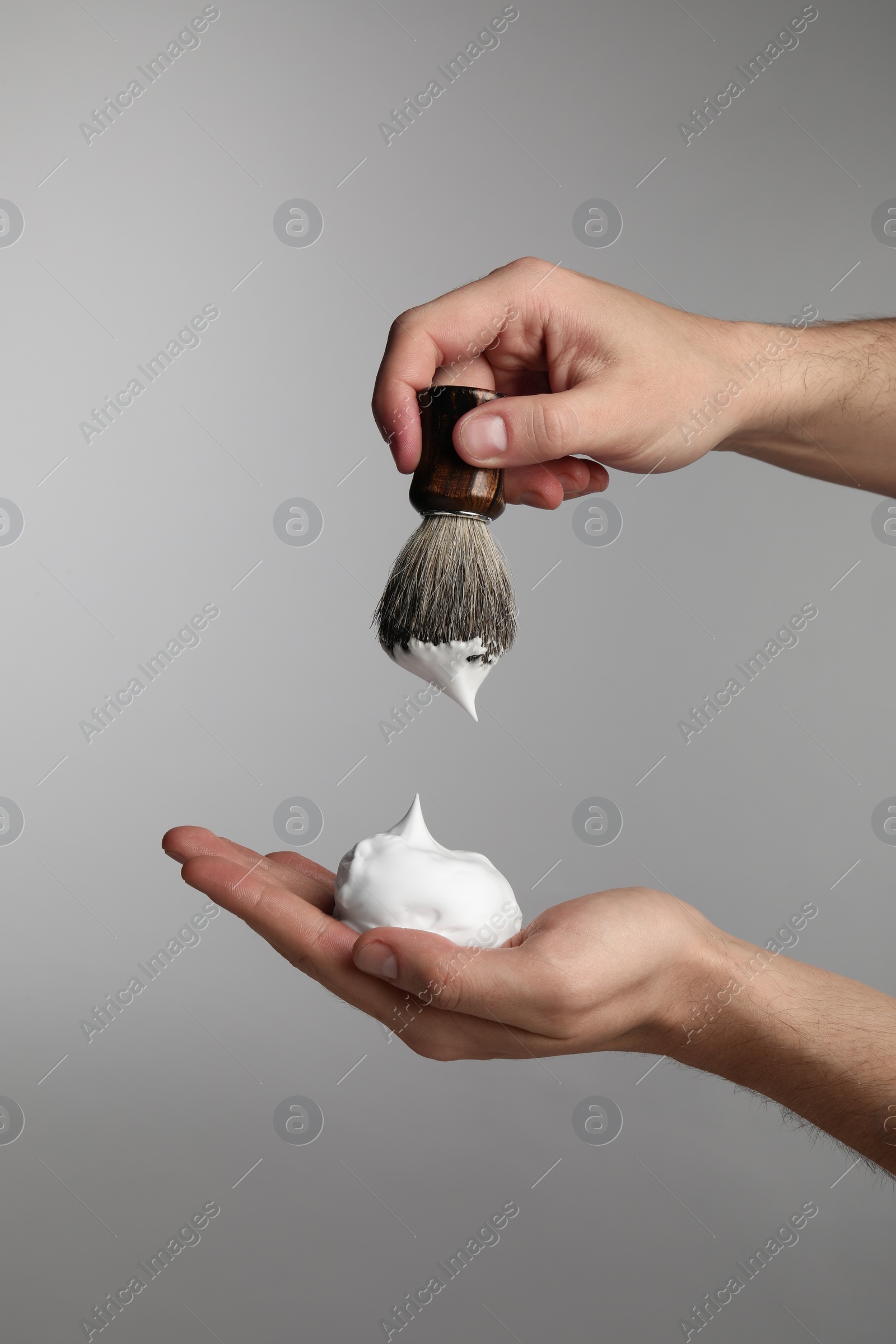 Photo of Man applying shaving foam onto brush on light grey background, closeup