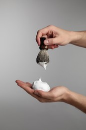 Man applying shaving foam onto brush on light grey background, closeup