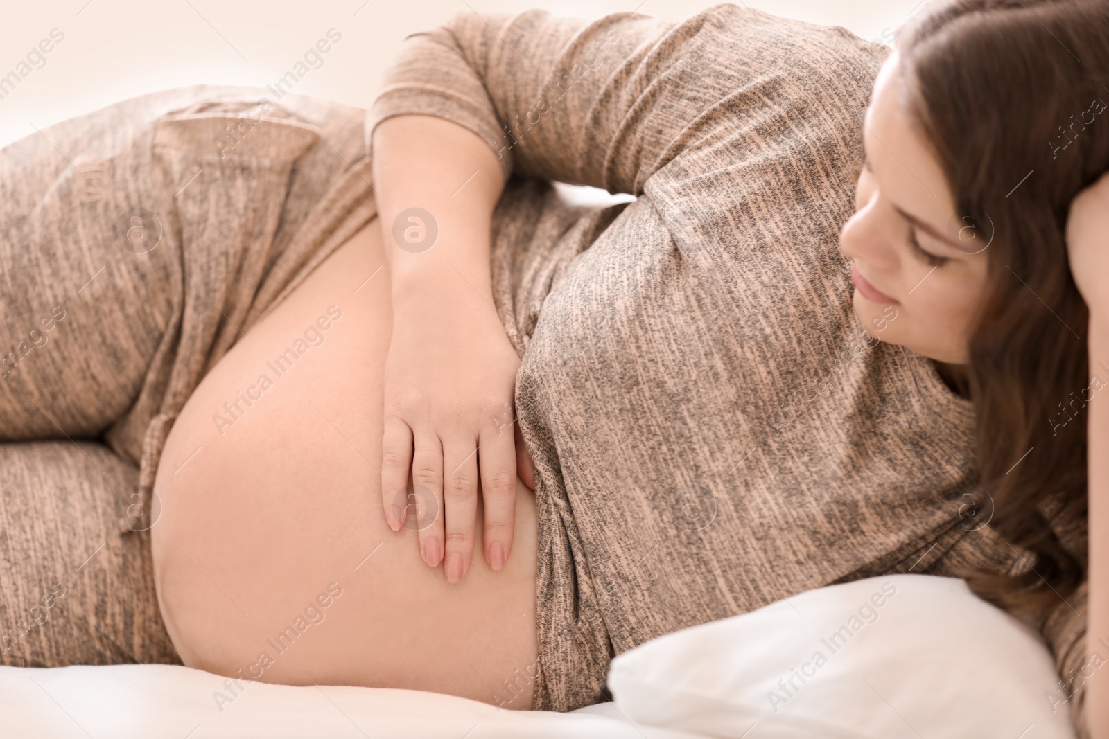 Photo of Young pregnant woman lying on bed at home